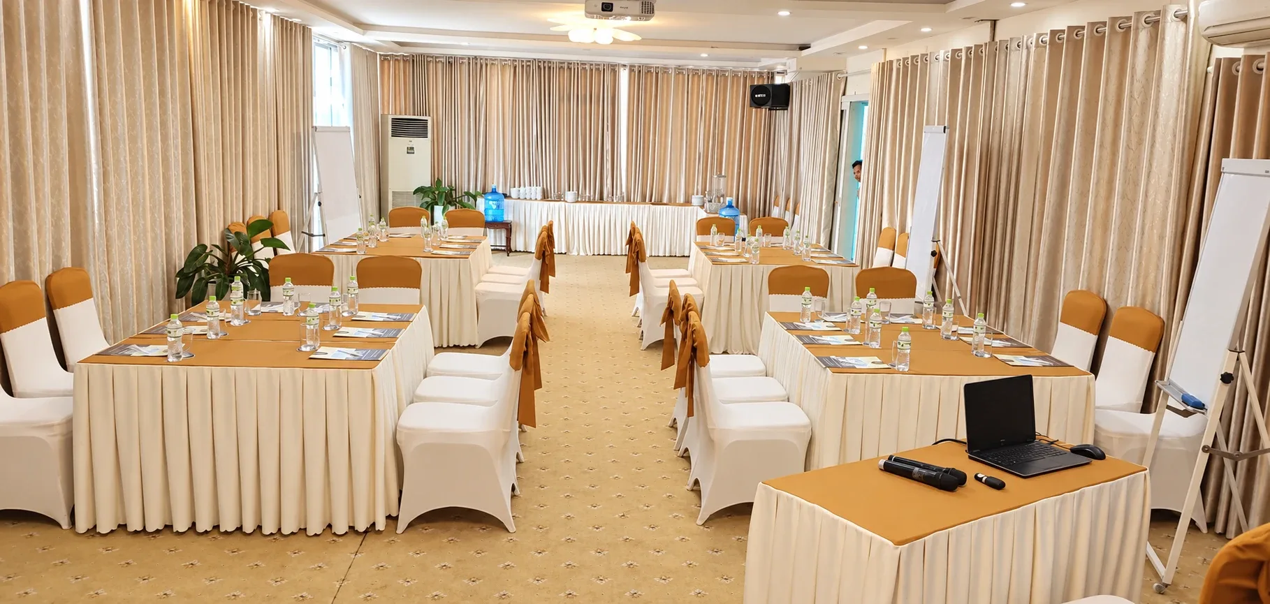 Bàn nhóm kê hai bên lối đi giữa, máy tính và micro không dây đặt trên bàn điều hành